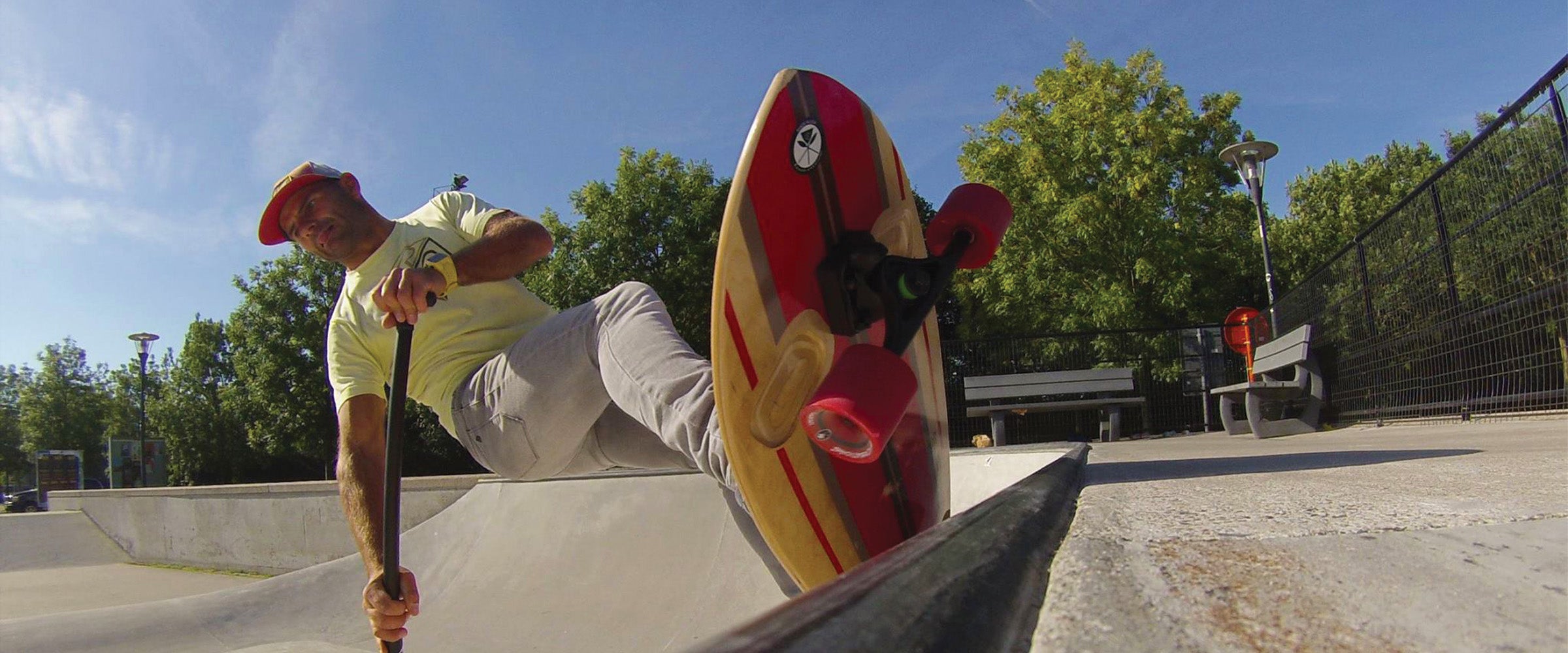 Man riding Kahuna Creations Shaka Longboard with 180mm trucks, 70mm wheels and ABEC7 bearings. Using an adjustable land paddle big stick skate pole.