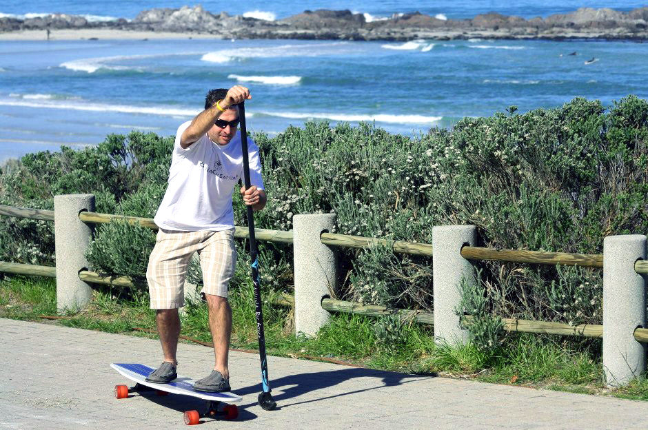 Man riding Kahuna Creations Bombora longboard with land paddle.