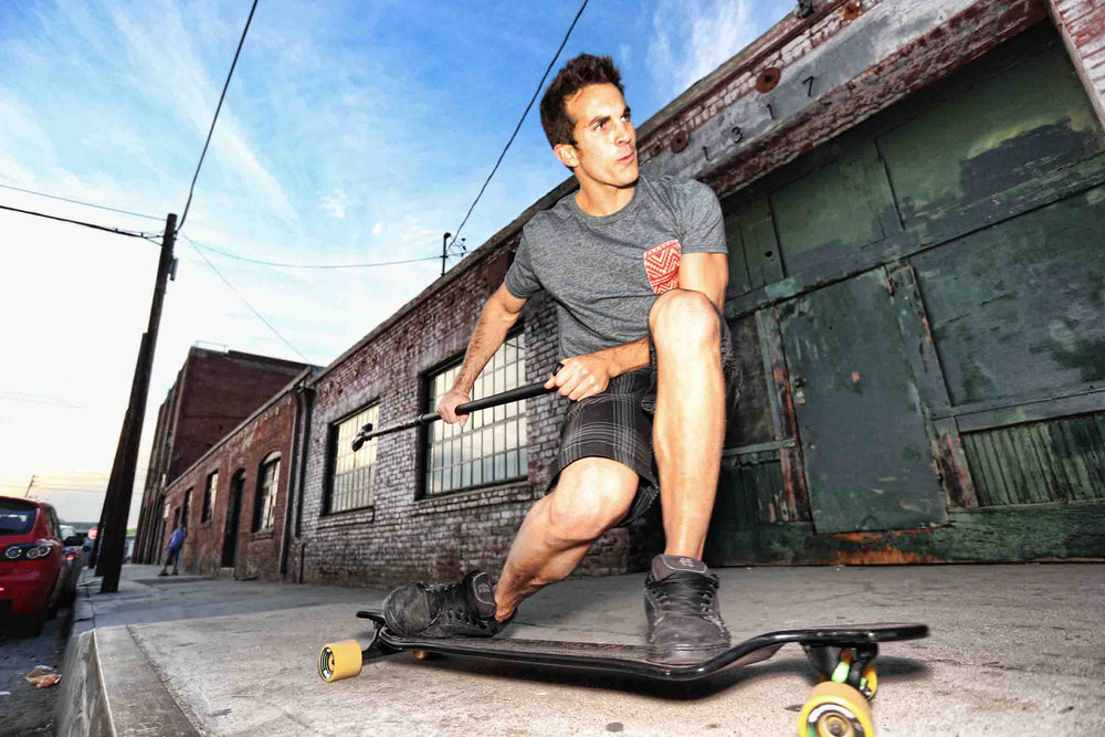 Man riding Kahuna Creations Blackwave drop deck longboard with land paddle.