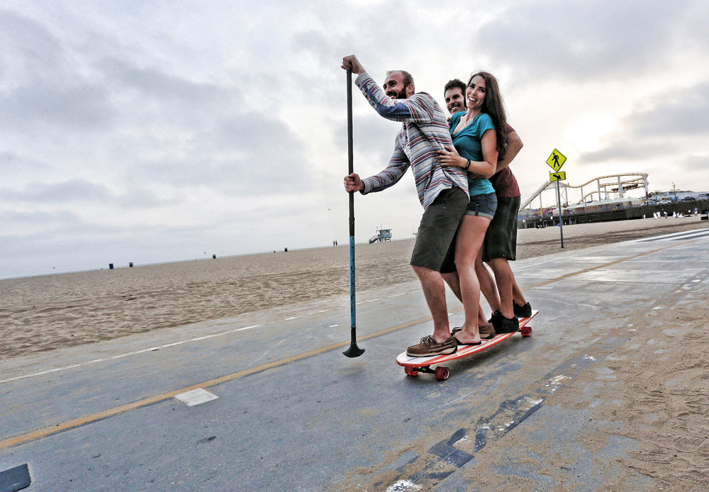 3 people riding Kahuna Creations Bombora longboard with land paddle.