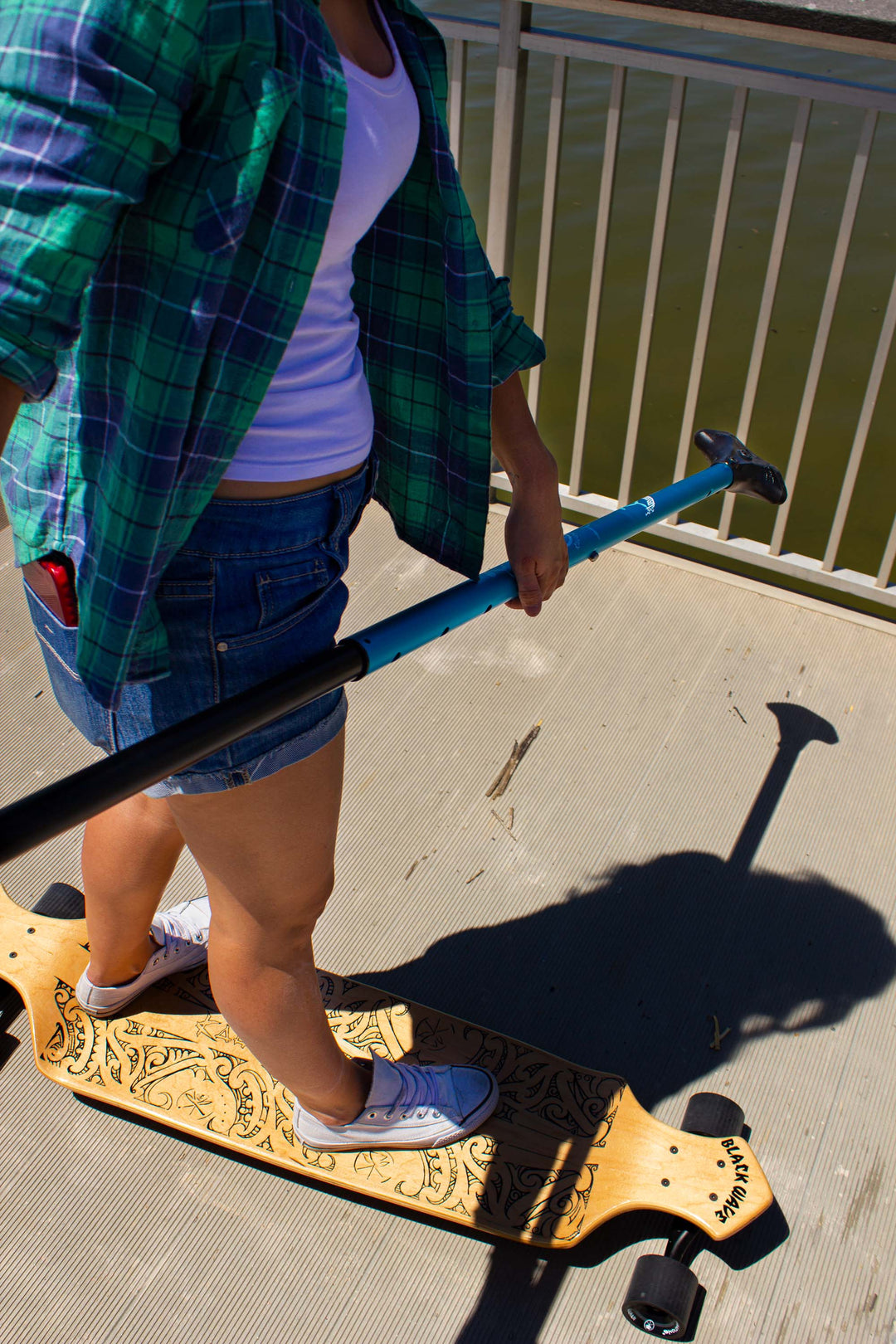 Woman riding Kahuna Creations drop deck longboard with land paddle.