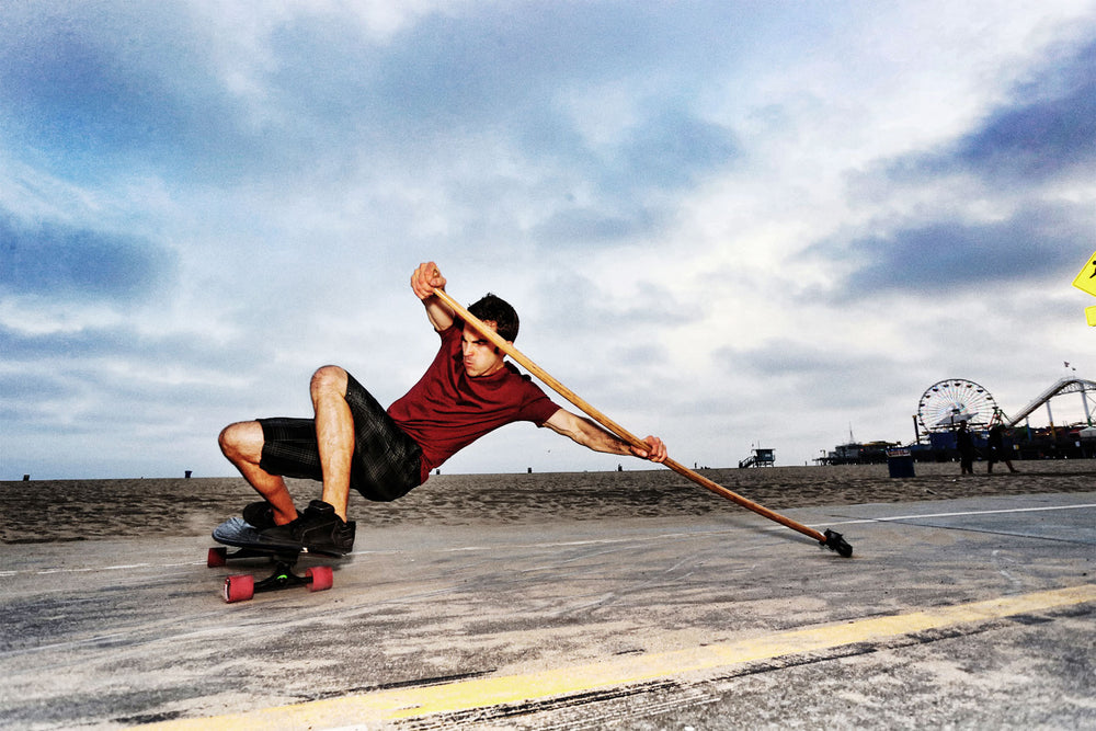 Man riding Kahuna Creations Shaka fishtail longboard with land paddle