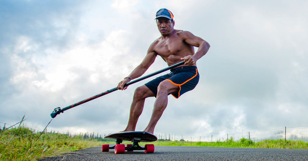 Man riding Kahuna Creations Shaka fishtail longboard with land paddle