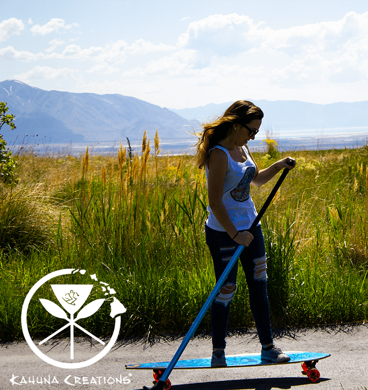 Woman riding Kahuna Creations Haka Sea Dragon longboard with land paddle.