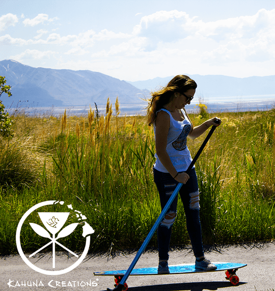 Woman riding Kahuna Creations Haka Sea Dragon longboard with land paddle.