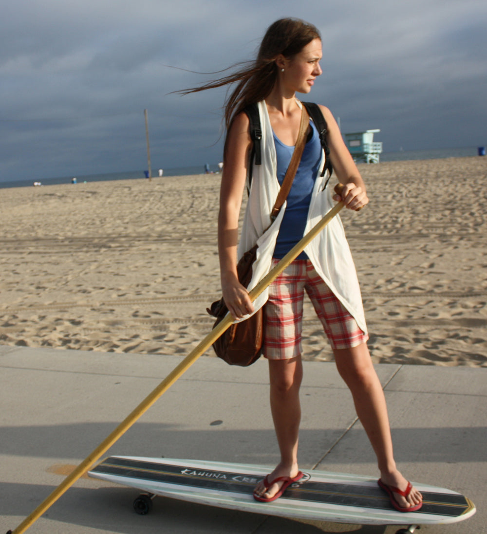 Woman riding Kahuna Creations Bombora longboard with land paddle.