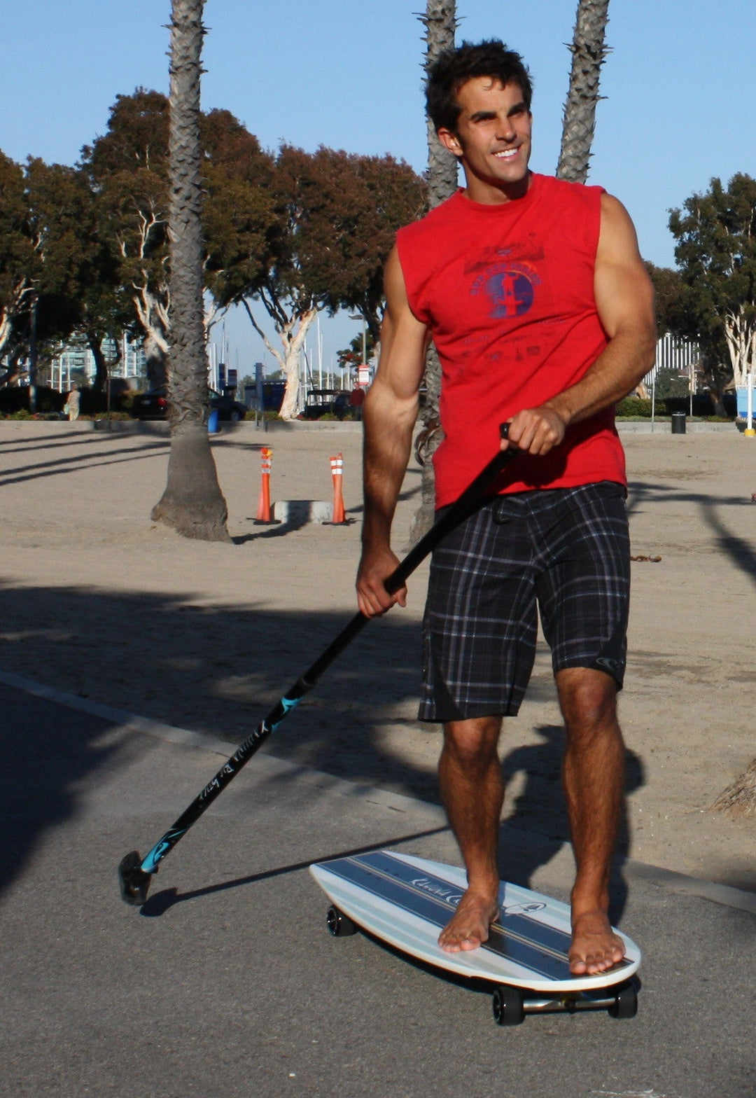 Man riding Kahuna Creations Bombora longboard with land paddle.