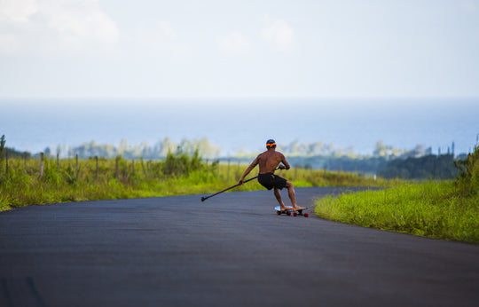 Man riding Kahuna Creations Shaka longboard with land paddle.