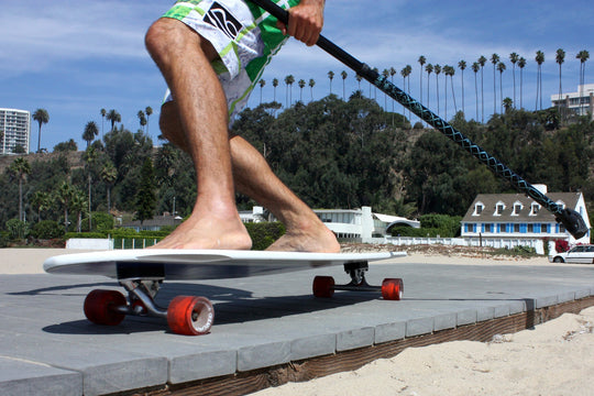 Man riding Kahuna Creations Bombora longboard with land paddle.